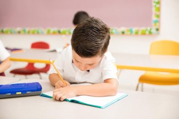 male-preschooler-wearing-uniform-working-writing-assigment-classroom_662251-2625